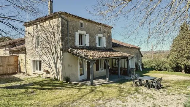La façade, la terrasse couverte et la table de jardin au soleil